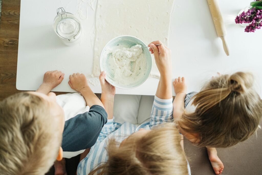 Three children mixing ingredients for homemade pastry in a bright kitchen setting.